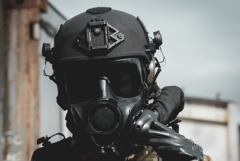 Tactical operator wearing an Avon Protection respirator and ballistics helmet during field training.