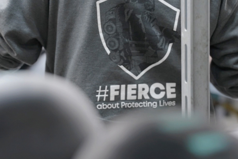 A close-up of the back of a grey sweatshirt featuring a shield logo and the text "#FIERCE about Protecting Lives."