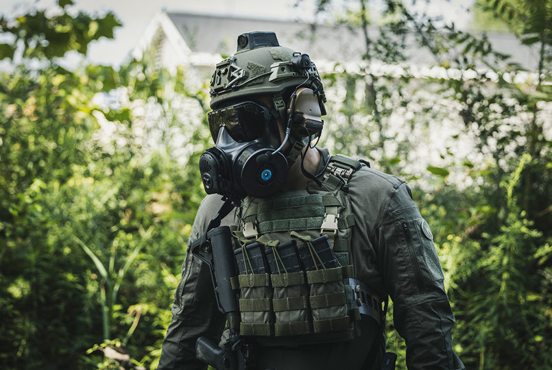 Two tactical operators in black uniforms and ballistic helmets wearing full-face respirators in an outdoor setting.