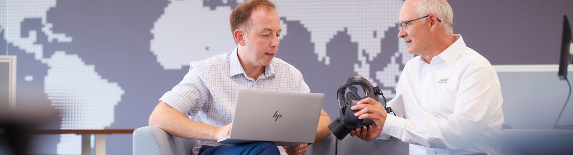 Two employees sat in an office looking at a respirator and laptop